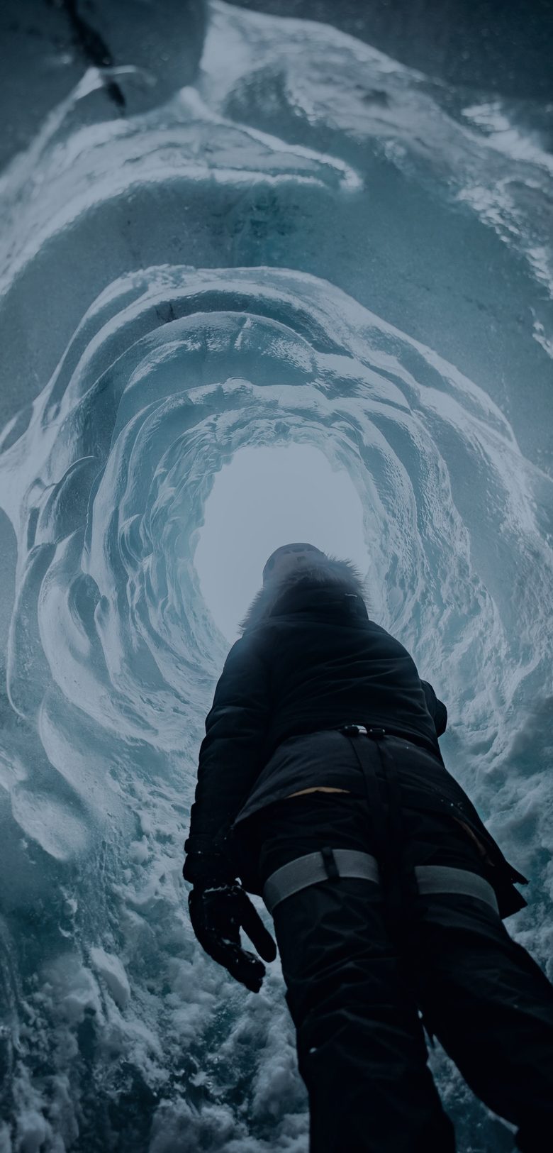A lone figure inside an Icelandic glacier cave, looking up to the opening